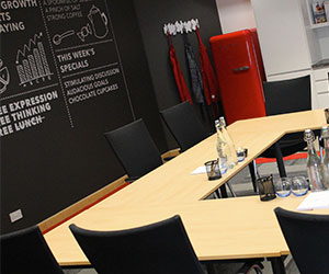 A creative kitchen meeting room with a U-shape table layout, with kitchen features including a fridge along the wall